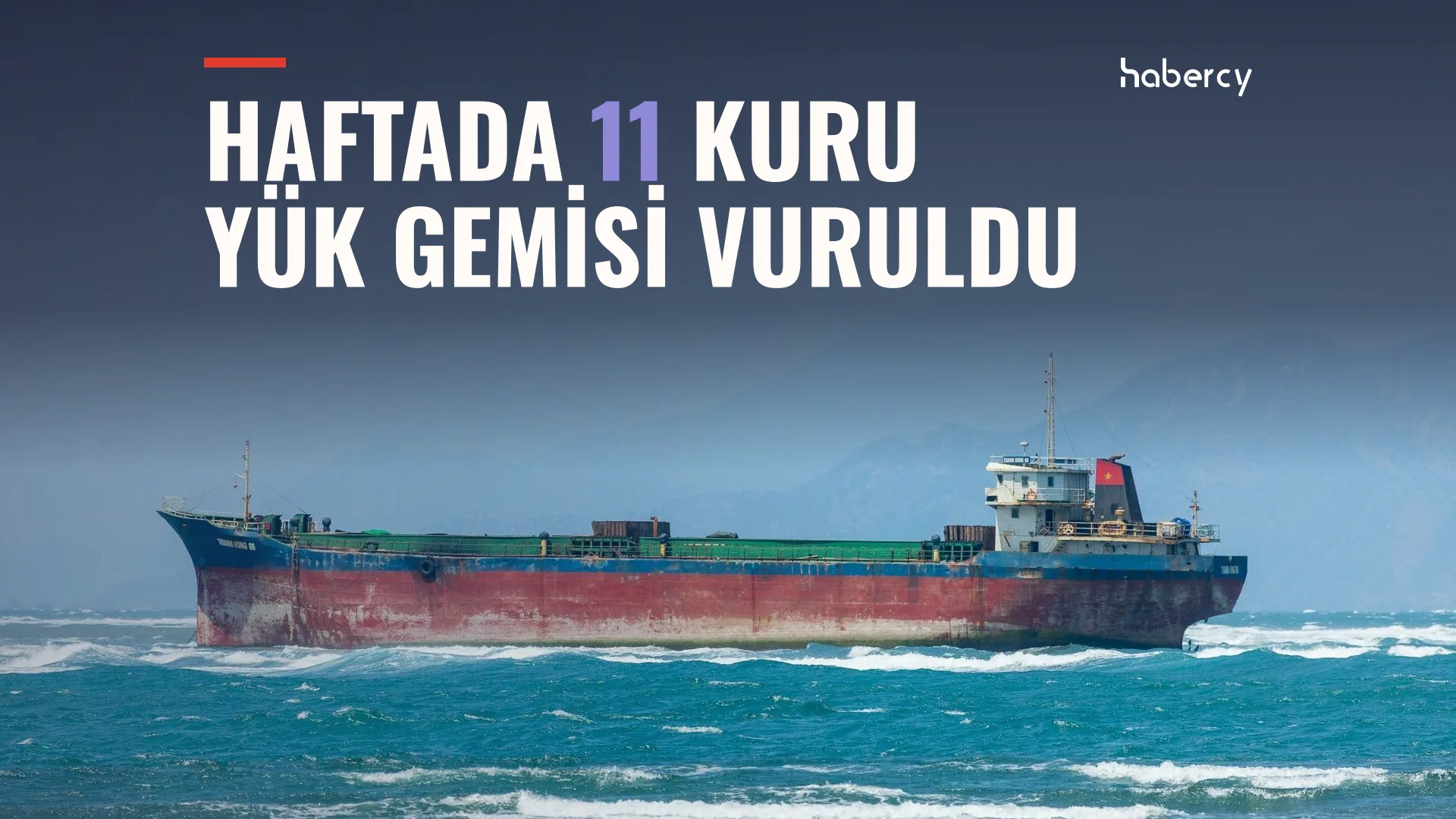 Dalgalı denizde kırmızı-lacivert gövdeli büyük bir kuru yük gemisi, arkada bulutlu gökyüzü