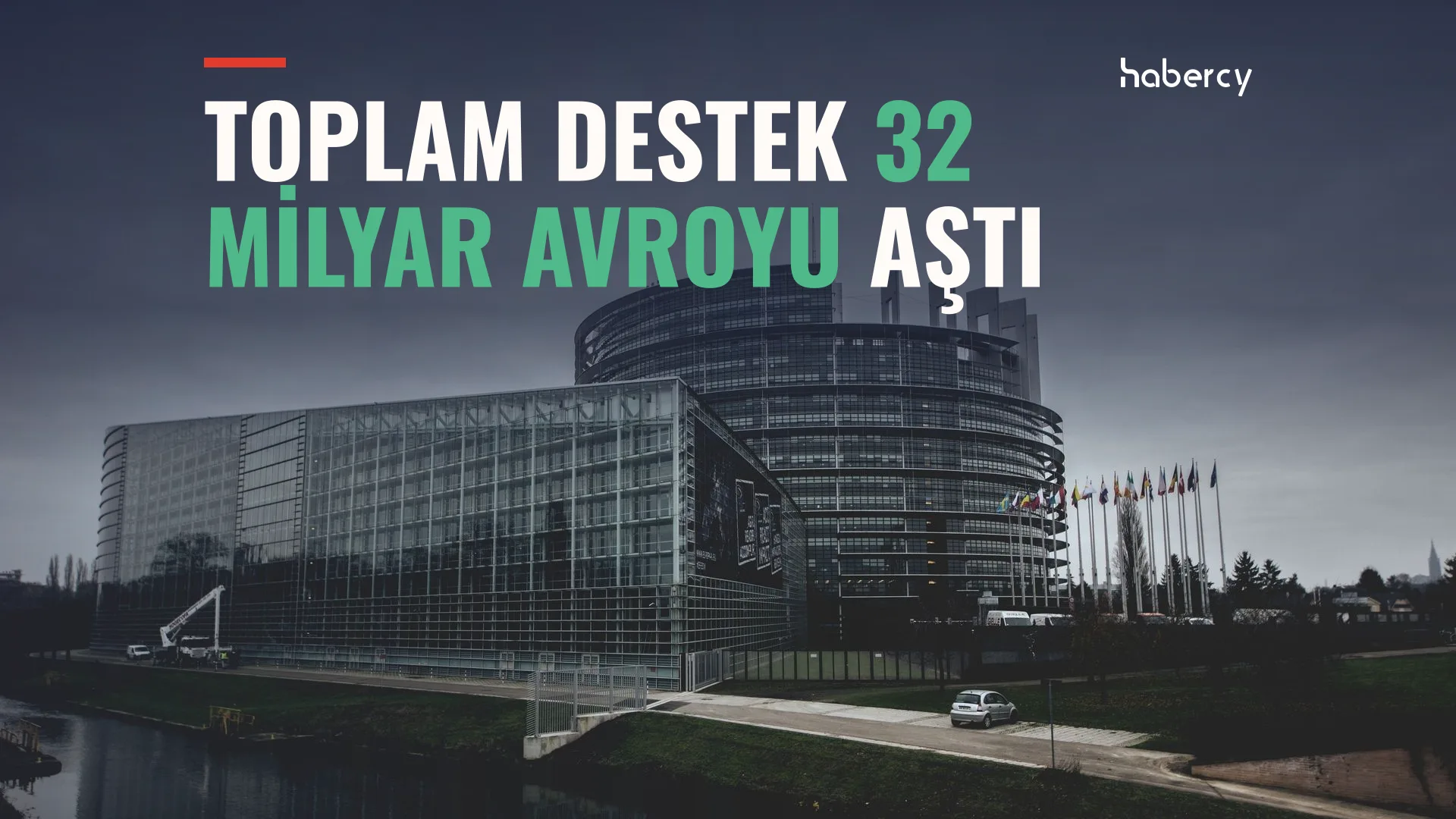 Kanal kıyısında cam cepheli yuvarlak Avrupa Parlamentosu binası ve önünde bayrak direkleri