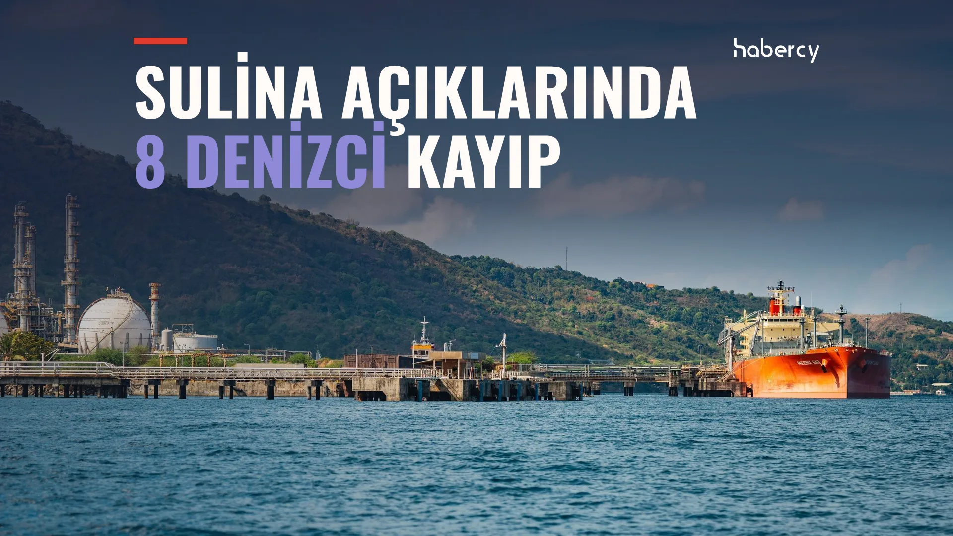 Tepelerin önünde rafineri iskelesine yanaşmış turuncu gövdeli bir tanker gemisi
